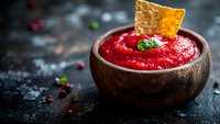 Fresh cranberry sauce with mint garnish served in wooden bowl, topped with crispy cracker on dark rustic background with scattered berries.