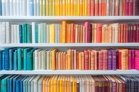 Colorful books arranged by spectrum on white shelves, creating vibrant rainbow pattern for library, bookstore, or home decor.