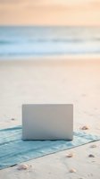 Laptop computer on blue towel at sandy beach during golden hour sunset, remote work and digital nomad lifestyle concept.