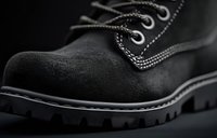 Close-up of black suede work boot with lug sole and metal eyelets, showcasing rugged footwear design for construction, labor, and outdoor professional use.