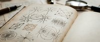 Open vintage notebook with hand-drawn geometric star patterns and compass designs on aged paper, surrounded by antique drawing tools for creative projects.