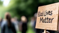 Wooden protest sign with handwritten text against blurred crowd background showing social activism and peaceful demonstration for racial equality and justice.