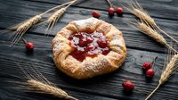 Freshly baked pastry with cherry jam and powdered sugar on rustic wooden background with wheat stalks and cranberries for bakery and food photography.