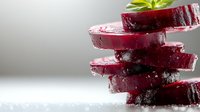 Fresh beetroot slices stacked with water droplets and green leaves on white background for healthy cooking and nutrition concepts.