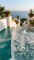 Sparkling water glass with bubbles on luxury poolside terrace overlooking ocean view, tropical vacation resort setting for summer refreshment concepts.