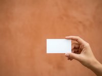 Hand holding blank white business card against warm terracotta textured wall background, suitable for branding, marketing mockups, and corporate identity presentations.