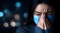 Young Asian woman wearing protective face mask touching nose bridge showing headache or stress with blurred city lights background at night.