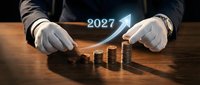 Businessman hands protecting growing coin stacks with 2027 arrow showing financial growth and investment planning for future success.