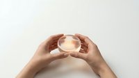 Hands holding glowing crystal ball with warm light emanating from center against neutral background for fortune telling and mystical concepts.
