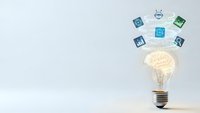 Glowing lightbulb with brain inside surrounded by floating technology icons on white background representing innovation and creative thinking in business.
