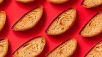 Fresh baked bread slices arranged in diagonal pattern on vibrant red background. Artisan bakery products for food photography and culinary designs.