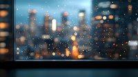 Blurred city skyline view through rain-covered window with bokeh lights creating dreamy atmosphere. Urban nightscape with water drops and glowing buildings in background.