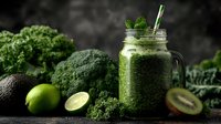 Fresh green smoothie with kale, broccoli, lime and kiwi in mason jar. Healthy detox drink surrounded by organic vegetables on dark background for wellness lifestyle.