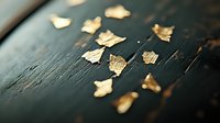 Delicate gold leaf fragments scattered on dark wooden surface create elegant contrast and texture, suitable for luxury branding and design projects.