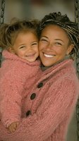 African American mother and mixed race daughter share genuine laughter while wearing matching pink fuzzy sweaters, expressing pure joy and family connection.