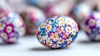 Decorative Easter egg with delicate floral pattern featuring pink, blue and purple flowers painted on white surface, shallow depth of field creates soft background blur.