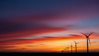 Wind turbines silhouetted against dramatic sunset sky with vibrant orange and purple clouds. Renewable energy concept for environmental projects.