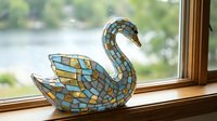 Decorative mosaic swan figurine with blue and gold tiles sitting on wooden windowsill overlooking serene lake view for home decor and interior design projects.