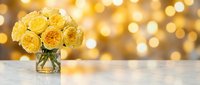 Yellow roses bouquet in glass vase on white table with golden bokeh lights background for romantic occasions and home decor.