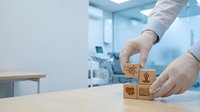 Healthcare professional arranging wooden blocks with medical icons in modern clinic environment for patient care planning and treatment organization.