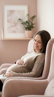 Pregnant woman relaxing in comfortable armchair at home, expecting mother in cozy sweater touching belly, maternity lifestyle and wellness concept.