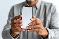 Senior man with dark skin holding smartphone with blank white screen against light background, showcasing modern technology use.