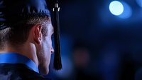 Graduate student in profile view wearing mortarboard cap against dark blue background with glowing moon, capturing contemplative moment at night graduation ceremony.