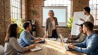 Diverse team of professionals collaborating in modern loft office space with exposed brick, natural light, and whiteboard during business meeting and brainstorming session.