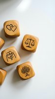 Wooden dice with engraved symbols including hearts, scales of justice, hands, and tree on white background for mindfulness and decision making games.