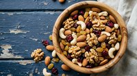 Mixed nuts and dried fruits in wooden bowl on rustic blue table. Healthy snacking, organic food ingredients for cooking and baking recipes.