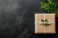 Eco-friendly gift wrapped in kraft paper with white string and fresh green leaves on dark background. Minimalist sustainable present packaging concept.