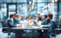 Blurred business meeting in modern conference room with professionals discussing strategy around table with warm bokeh lighting effects.