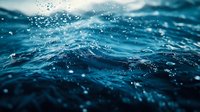 Dramatic close-up of dark blue ocean waves with water droplets splashing in sunlight creating dynamic texture and movement. Moody seascape for nature backgrounds.