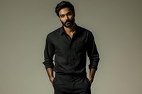 Confident South Asian man in elegant black shirt with hands in pockets against neutral background, portraying professional masculinity.