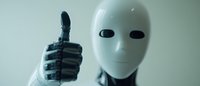 White robotic figure giving thumbs up gesture against blurred background, representing artificial intelligence and positive technology advancement.