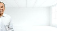 Middle-aged man with South Asian ethnicity wearing white business shirt smiling in bright modern office space with minimalist interior design.