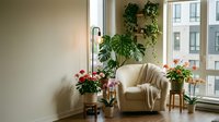 Cozy living room corner with beige armchair, houseplants and flowers by large window. Modern apartment interior design with natural light and greenery.