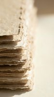Stack of aged handmade paper sheets with rough torn edges and natural texture in warm beige tones for craft and artistic projects.