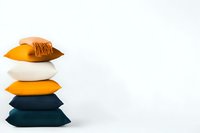 Stack of minimalist decorative pillows in orange, white and dark teal colors arranged vertically against white background, modern interior design element.