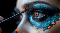 Dramatic turquoise and orange eye makeup application with professional brush. Extreme macro shot showing intricate details of creative cosmetics artistry and precise application technique.