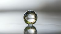 Transparent glass sphere with golden yellow tint reflecting on glossy surface creating mirror effect against soft gradient background for luxury design concepts.