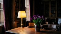 Elegant home library interior with purple tulips, warm lamp lighting, leather furniture and wooden bookshelves creating cozy reading atmosphere.