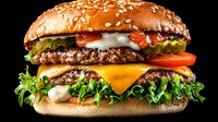Fresh double cheeseburger with beef patties, melted cheddar, lettuce, tomatoes, onions and sauce on sesame bun against black background. Appetizing fast food.