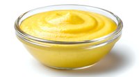 Creamy yellow mustard sauce in transparent glass bowl, smooth texture with swirl pattern on surface for culinary use in sandwiches and recipes.