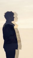Young man with dark curly hair, Caucasian ethnicity, wearing casual dark clothing, shown in profile silhouette merged with a serene beach landscape, representing introspection, duality, and inner contemplation for mental health and wellness concepts.