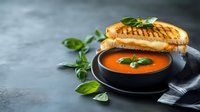 Grilled cheese sandwich with melted mozzarella served alongside creamy tomato basil soup in black bowl, garnished with fresh basil leaves on dark background.