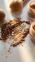 Loose bronze and gold shimmer powder scattered on white surface with makeup brushes and containers, suitable for cosmetics, beauty, and makeup artistry applications.