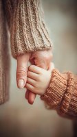 Close-up of adult and child hands holding together wearing matching beige knit sweaters showing family bond and warmth in soft natural lighting.