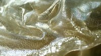 Shimmering gold silk fabric with elegant folds and creases creates luxurious texture and light reflection pattern, suitable for fashion and luxury backgrounds.