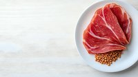 Raw sliced prosciutto ham with chickpeas on white ceramic plate against light background. Perfect for food blogs and culinary publications.